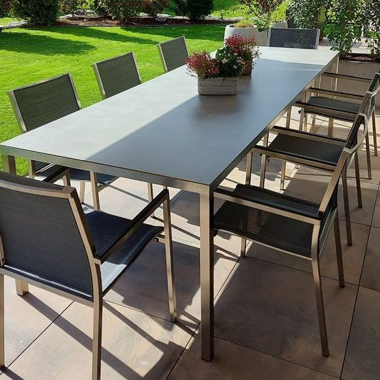Eine Outdoor-Essplatz mit einem langen Tisch und sechs Stühlen, mit Pflanzen und Blumen auf dem Tisch.