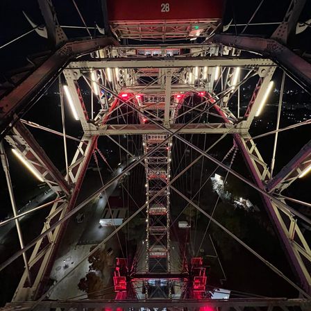 Ein Riesenrad bei Nacht mit roten Lichtern und der Nummer 28 sichtbar auf der Spitze. Die Struktur ist aus Metall mit mehreren Balken und Seilen.