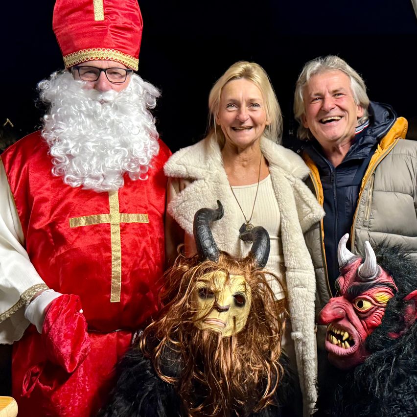 Drei Menschen in Festtagskostümen, eine Person in einem Weihnachtsmannkostüm, eine Frau und ein Mann mit Hörnern auf den Köpfen.