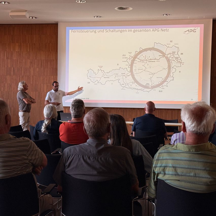 Ein Mann präsentiert eine Folie mit einer Karte während einer Präsentation in einem Klassenzimmer, während mehrere Menschen aufmerksam zuhören.
