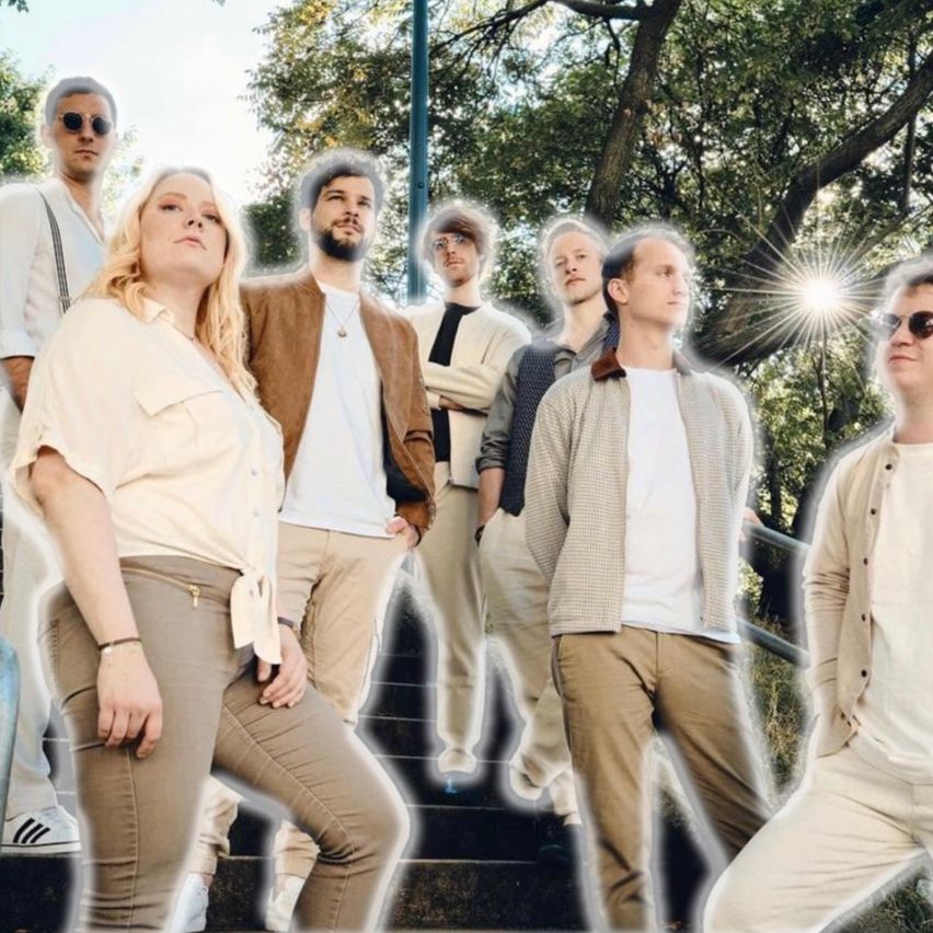 A group of people dressed in light colors, wearing sunglasses, stand on stairs under a tree in a park.