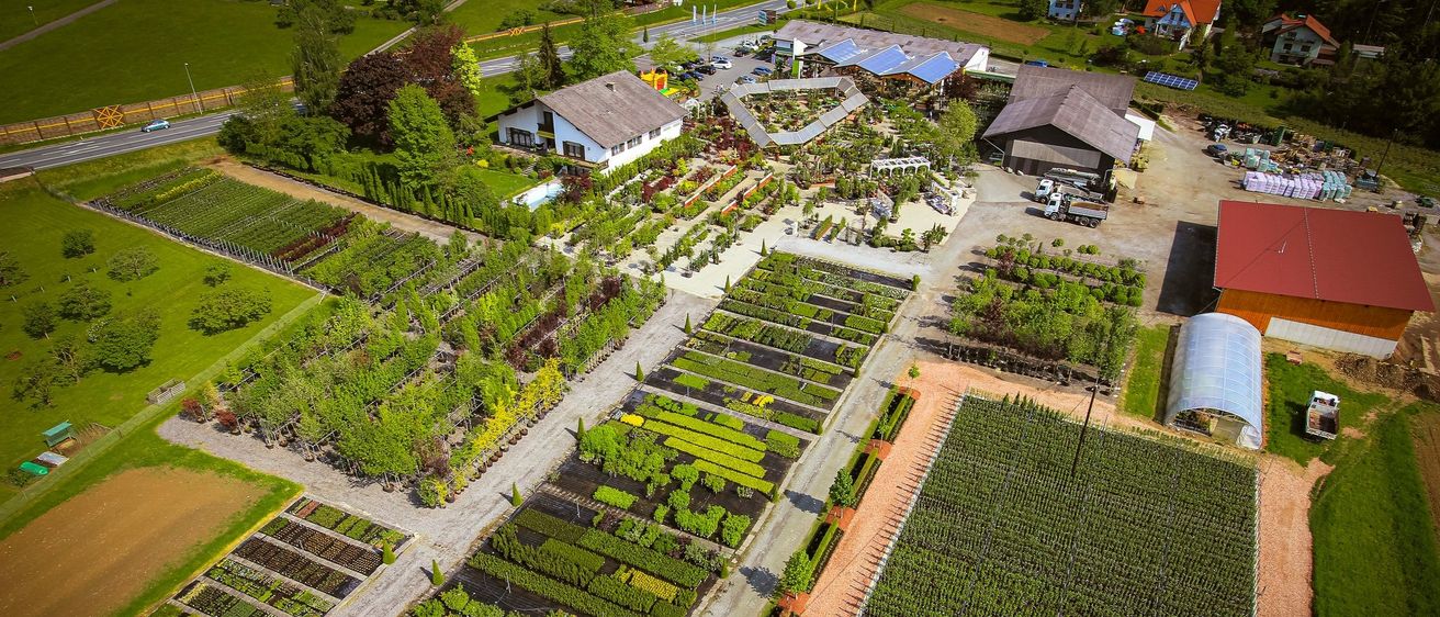 Eine Luftaufnahme eines Gartens mit vielen grünen Pflanzen und Bäumen. Ein großes Gebäude mit einem braunen Dach befindet sich in der Mitte. Ein Lastwagen ist auf dem Parkplatz geparkt.
