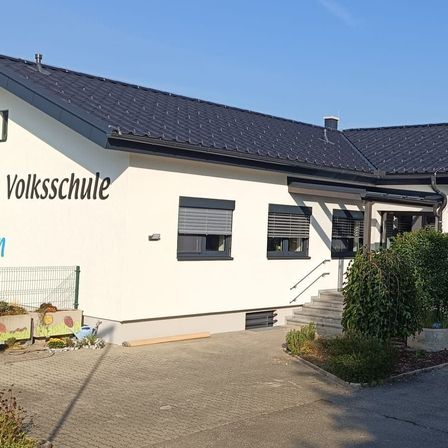 Ein weißes Haus mit schwarzem Dach, einer Einfahrt und einer Treppe, die zum Eingang führt. Das Haus hat einen Zaun, einen kleinen Busch und eine Topfpflanze.