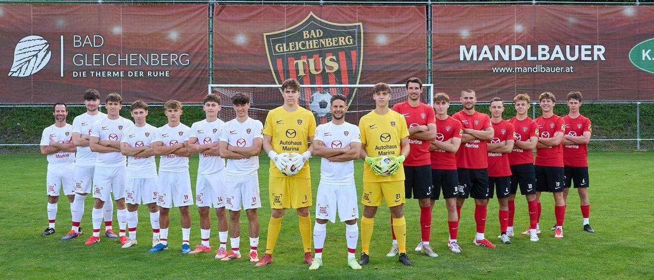 Eine Fußballmannschaft in gelben und weißen Trikots, zusammen mit roten und weißen Uniformen, posiert für ein Mannschaftsfoto auf einem grünen Feld mit Bannern dahinter.