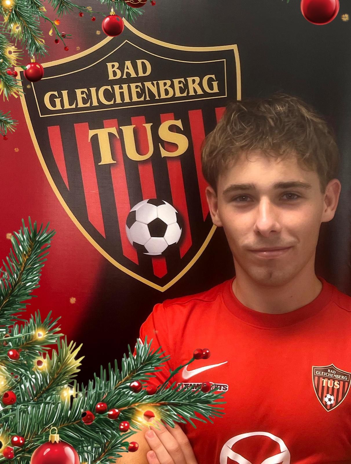 Ein Fußballspieler posiert für ein Foto vor einem Bad Gleichenberg-Klublogo, mit einem Weihnachtsbaum und einem Fußball im Hintergrund.
