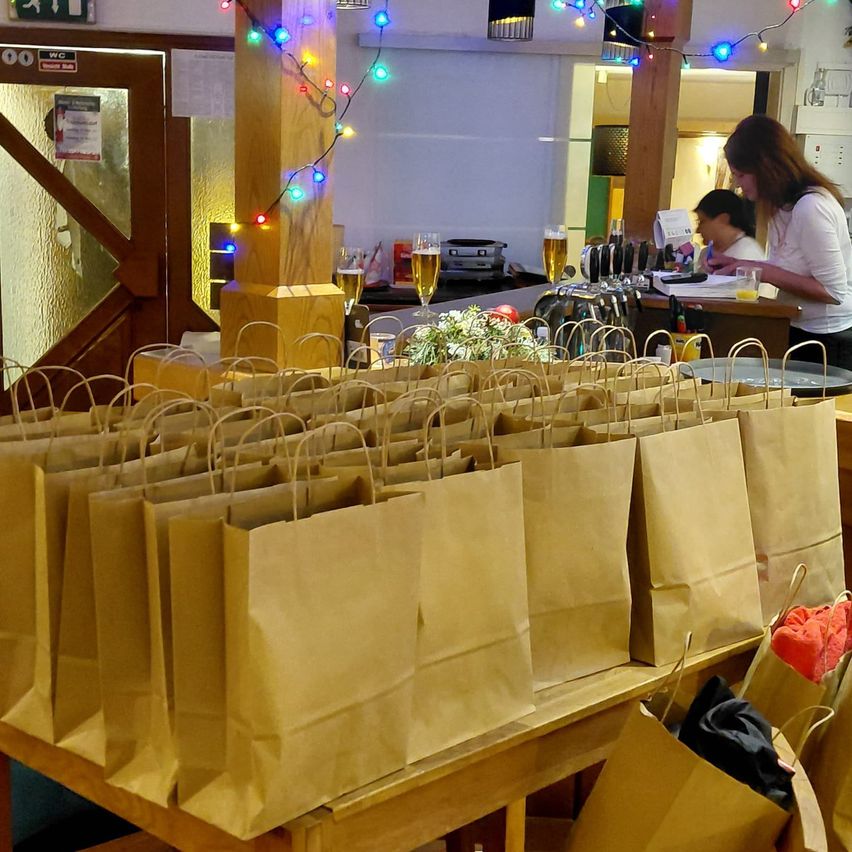 Eine Bartheke ist mit Papiertüten, bunten Lichtern und einer Blumenarrangement dekoriert. Eine Frau steht hinter der Theke, und ein Kind sitzt in der Nähe.