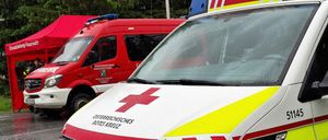 Zwei Ambulanzfahrzeuge, beide mit rotem Kreuz und gelben Reflektoren markiert, sind bei Regen geparkt. Das vordere Fahrzeug hat 'Osterreichisches Rotes Kreuz' auf seiner Motorhaube.