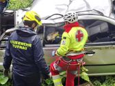 Rettungskräfte kümmern sich um eine Person in einem beschädigten Fahrzeug. Ein Helfer stabilisiert die Person, während ein anderer die Szene sichert.