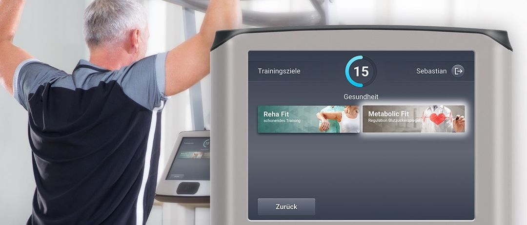 Ein älterer Mann benutzt ein Fitnessgerät in einem Fitnessstudio. Der Monitor zeigt 'Trainingsziele', '15' und 'Sebastian'. Der Bildschirm zeigt 'Reha Fit' und 'Metabolic Fit'. Unten befindet sich eine Taste mit der Aufschrift 'Zuruck'.