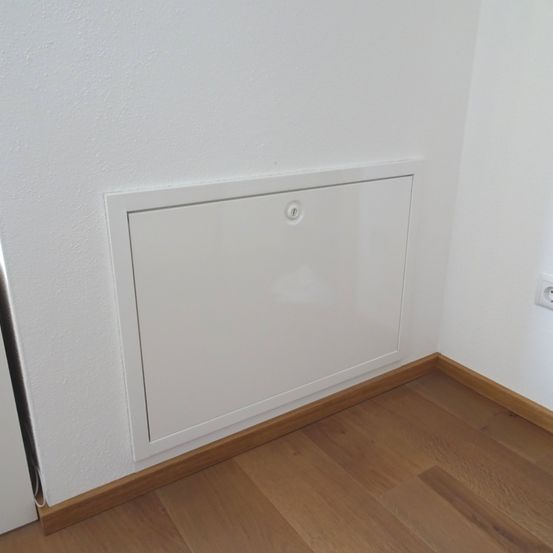 Eine weiße Tür mit einem silbernen Griff ist an der Ecke einer weißen Wand installiert. Der Boden ist aus Holz.