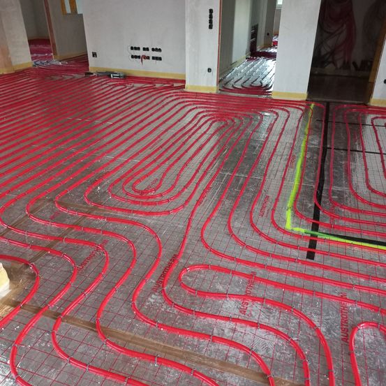 Ein leerer Raum mit einem roten Rohrsystem auf dem Boden und weißen Wänden. Der Boden ist sauber ohne sichtbare Möbel.