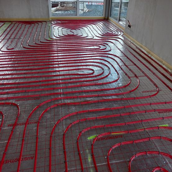 Ein Raum im Bau mit roten Rohren, die ein Rastermuster auf dem Boden und den Wänden bilden, zusammen mit Glasfenstern.