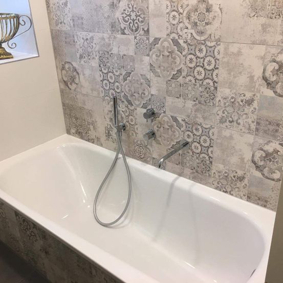 Ein modernes Badezimmer mit einer weißen Badewanne, verzierten Fliesenwänden und einer silbernen Duschbrause.