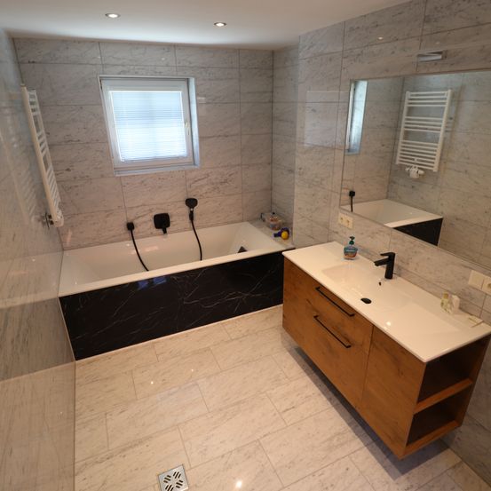 Ein modernes Badezimmer mit Marmorfliesen, einer Badewanne, einem Waschbecken, einem Spiegel und einem Handtuchhalter.