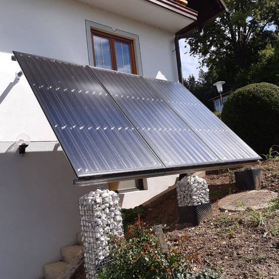 Solarmodule an der Außenwand eines Hauses montiert, darunter Pflanzen und Steine.