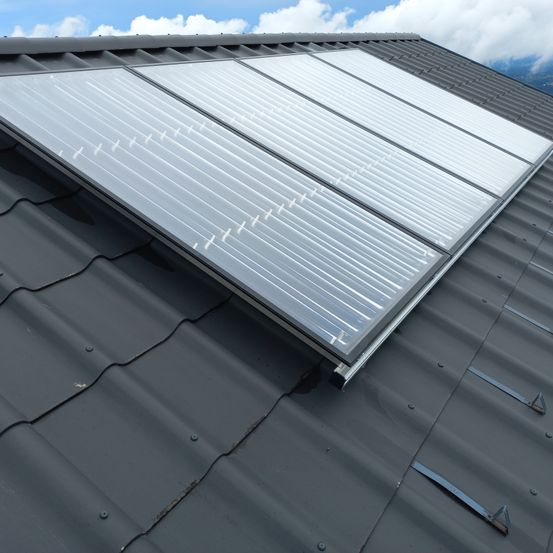 Sonnenkollektoren sind auf einem grauen Dach installiert, unter einem klaren blauen Himmel mit einigen Wolken.