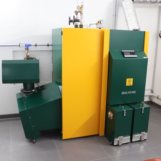 Eine grüne und gelbe Industrieeinheit mit der Aufschrift Multifire steht in einem Raum mit gefliestem Boden. Sie verfügt über ein digitales Bedienfeld und ist mit Rohren verbunden.