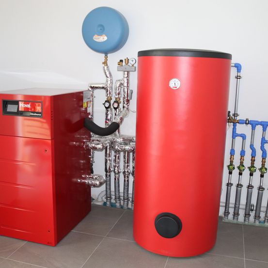 Ein roter und schwarzer Tank mit Messgeräten steht neben einer roten Box mit dem Wort Hova. Der Raum ist mit einer weißen Wand gefliest.