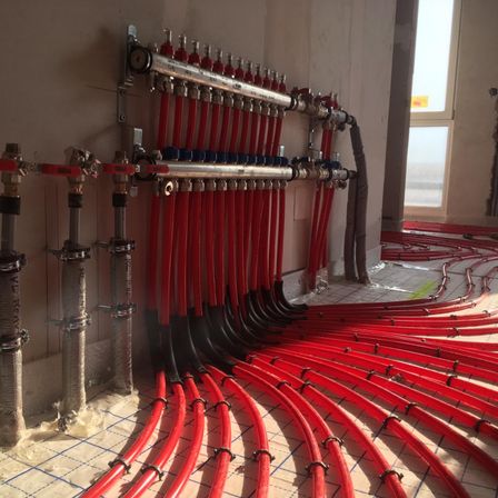 Eine Wand mit mehreren roten und silbernen Rohren, die daran befestigt sind. Die Rohre sind mit einem Fenster und einem gefliesten Boden verbunden.