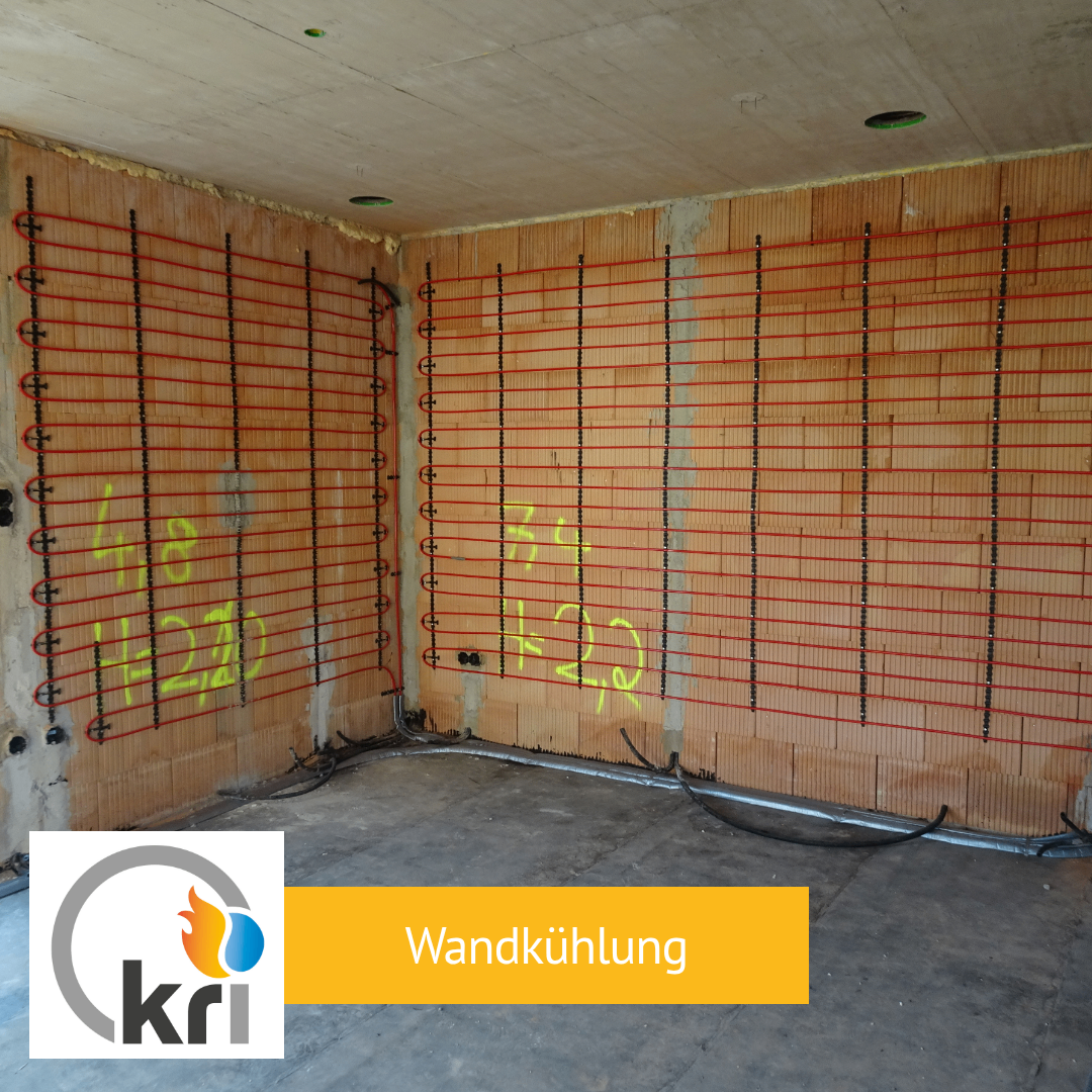 An interior construction site with red heating pipes and yellow markings on the walls. The floor is concrete and there is a logo with the text 'kRi' in the bottom left.
