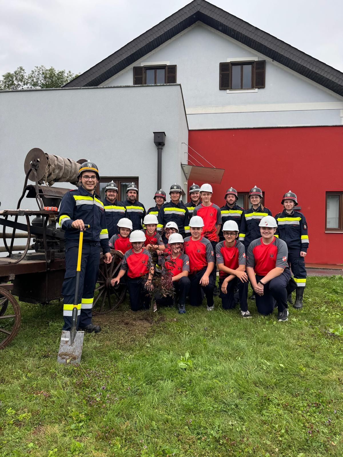 Eine Gruppe Feuerwehrleute posiert für ein Foto vor einem Feuerwehrauto und einem Gebäude.