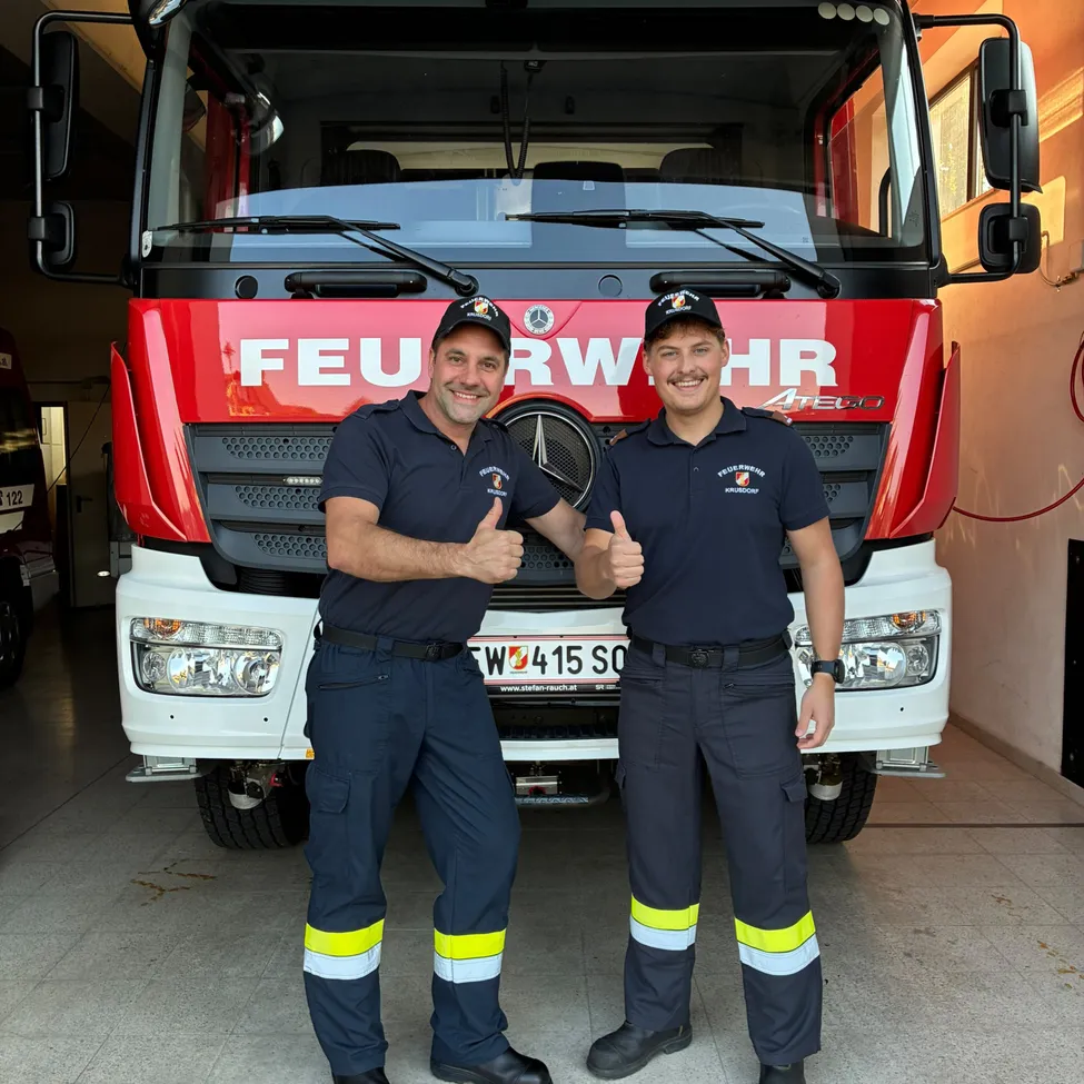 Zwei Männer in Uniform stehen vor einem roten Feuerwehrauto.