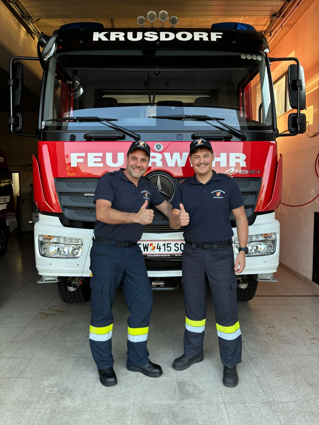Zwei Männer in Uniform stehen vor einem roten Feuerwehrauto.