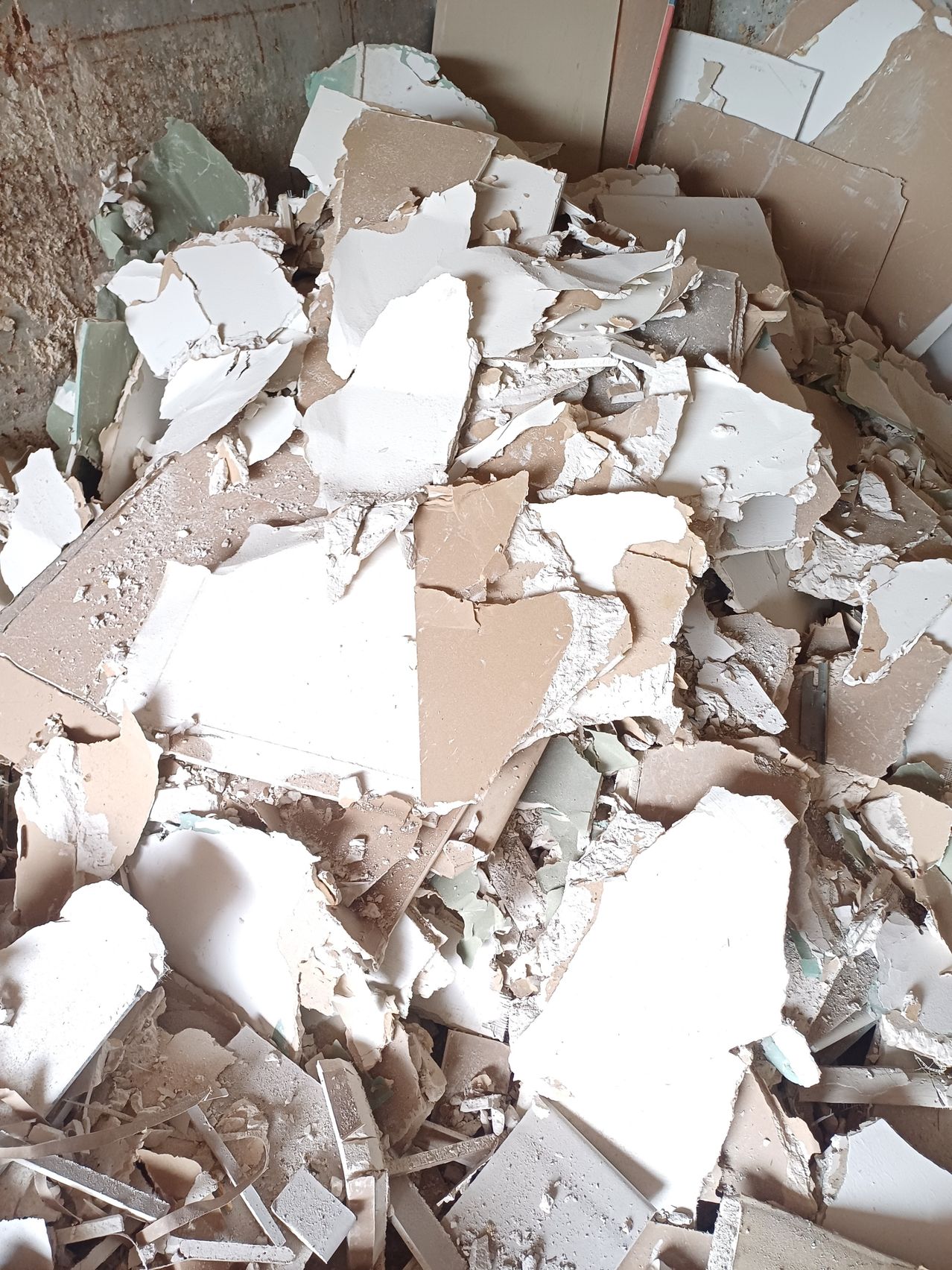 Ein Haufen zerbrochener Stücke von Gipskarton und Pappe liegt auf dem Boden verstreut, mit etwas Staub und Schmutz.