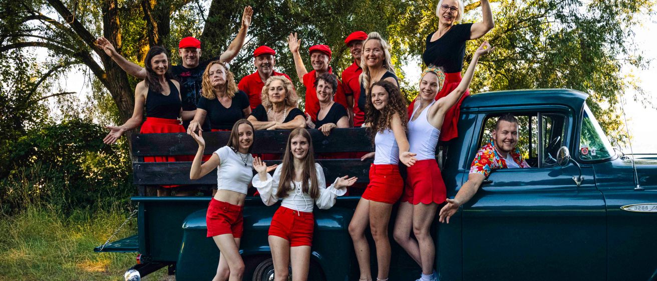 Eine Gruppe von Menschen in roten und weißen Kleidungsstücken steht im Heck eines grünen Pickup-Trucks. Sie lächeln und posieren für ein Foto.