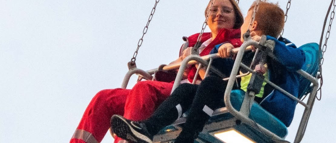 Eine Frau und ein junger Junge lächeln, während sie auf einer Schaukel in einem Vergnügungspark sitzen.