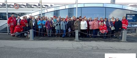 A group of people dressed in winter clothes pose for a photo in front of a building with flags and a red text overlay reading 'Rotes Kreuz Waidhofen/T'.