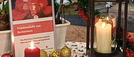 Eine Weihnachtsdekoration mit einer roten Kerze, einem Schild, das Friedenslicht aus Bethlehem steht, und einem Laternen mit brennender Kerze.