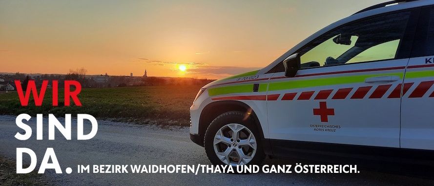 An ambulance with a red cross on the side is parked on a road with a sunset in the background. The text reads, 'We are in Waidhofen/Thaya and the whole of Austria.'