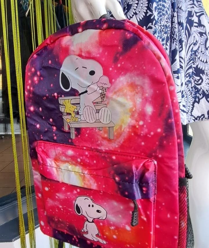 Ein rosa Rucksack mit einem Tie-Dye-Design, auf dem Snoopy auf einer Bank sitzend Eis isst. Ein weiterer Snoopy-Charakter ist auf der Vordertasche zu sehen.
