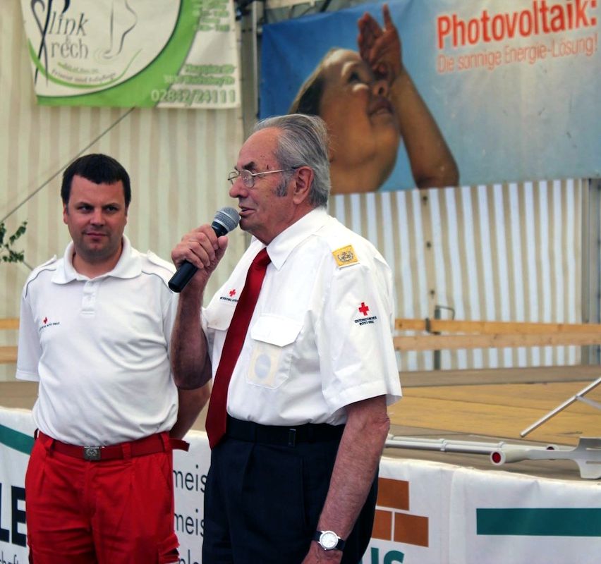 Zwei Männer auf der Bühne, einer spricht in ein Mikrofon. Ein Banner mit dem Text Photovoltaik im Hintergrund.