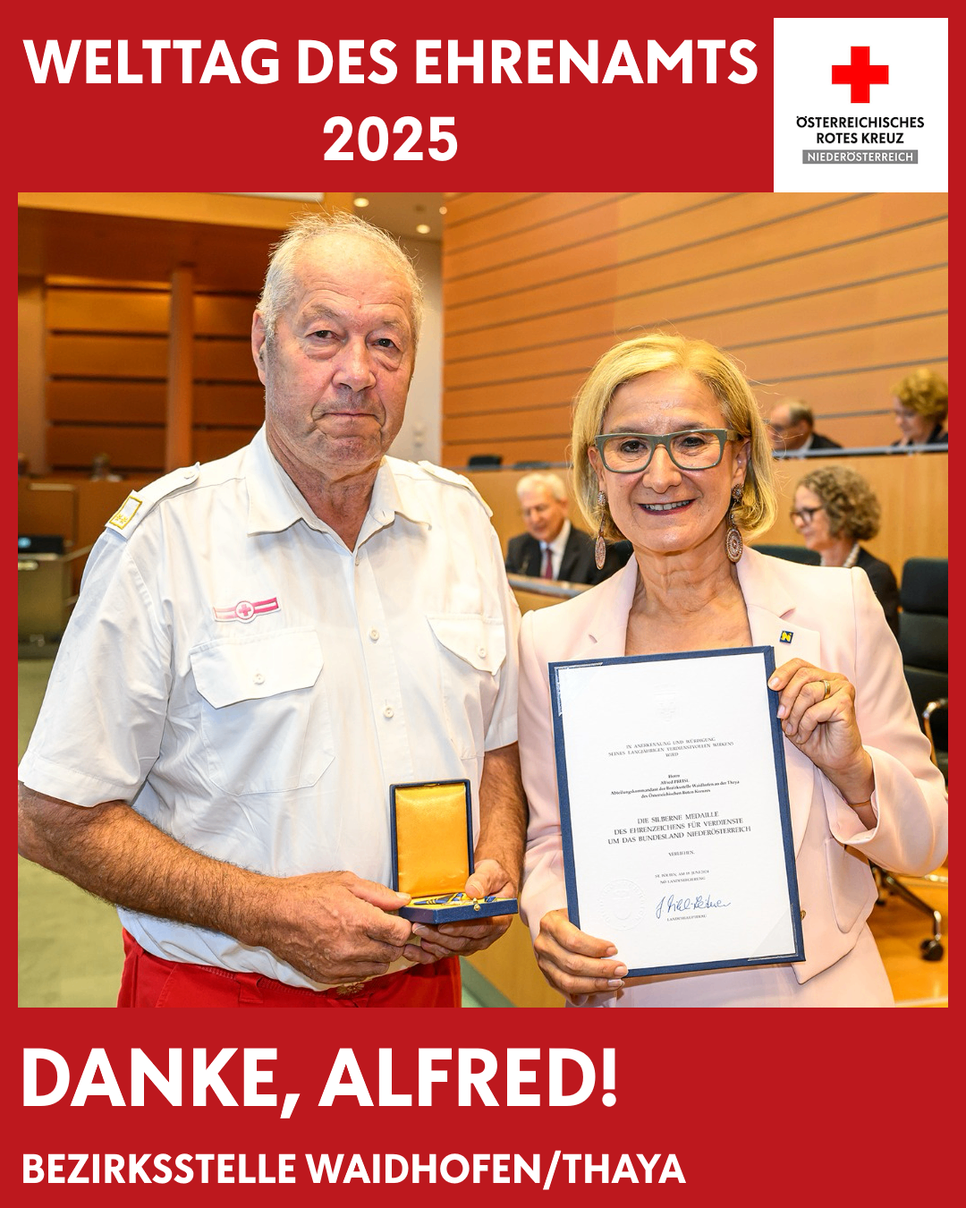 Ein Mann und eine Frau stehen zusammen und halten beide eine Medaille. Der Mann trägt eine weiße Uniform und die Frau ein rosa Kostüm. Sie stehen vor einem roten Hintergrund mit 'Danke Alfredi' und '2025' darauf. Dahinter ist ein verschwommenes Bild von Menschen, die auf Stühlen sitzen.