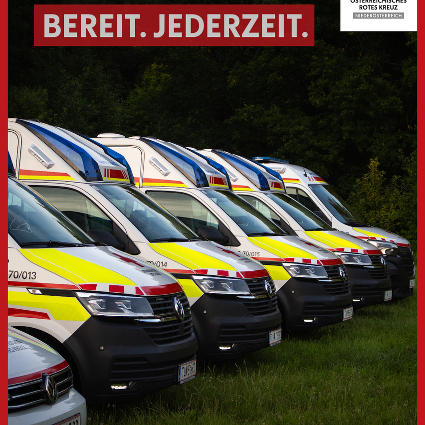 Eine Reihe von Krankenwagen mit roten, weißen und gelben Streifen, die auf einem Rasenparkplatz geparkt sind. Der Text 'BEREIT. JEDERZEIT.' ist prominent angebracht.