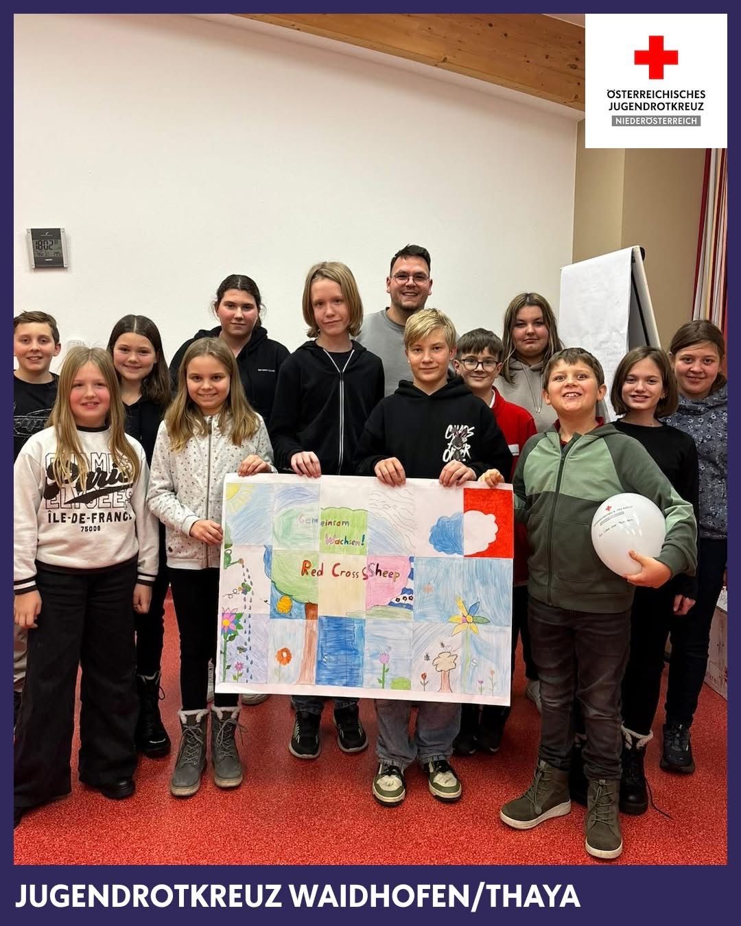 Eine Gruppe von Kindern und Erwachsenen posiert für ein Foto. Ein Kind hält eine Zeichnung eines roten Kreuzes. Die Kinder tragen Freizeitkleidung und die Erwachsenen haben Jacken an.