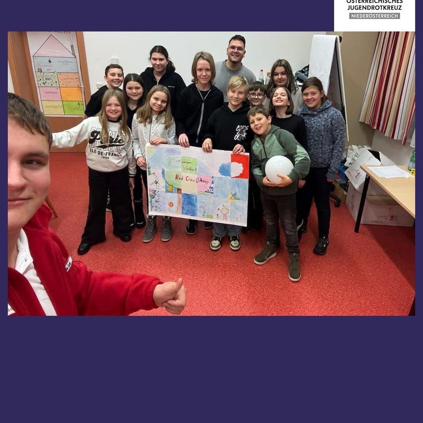 Eine Gruppe von Kindern und zwei Erwachsenen posiert für ein Foto in einem Raum. Ein Kind hält ein Poster. Sie tragen alle Winterkleidung.