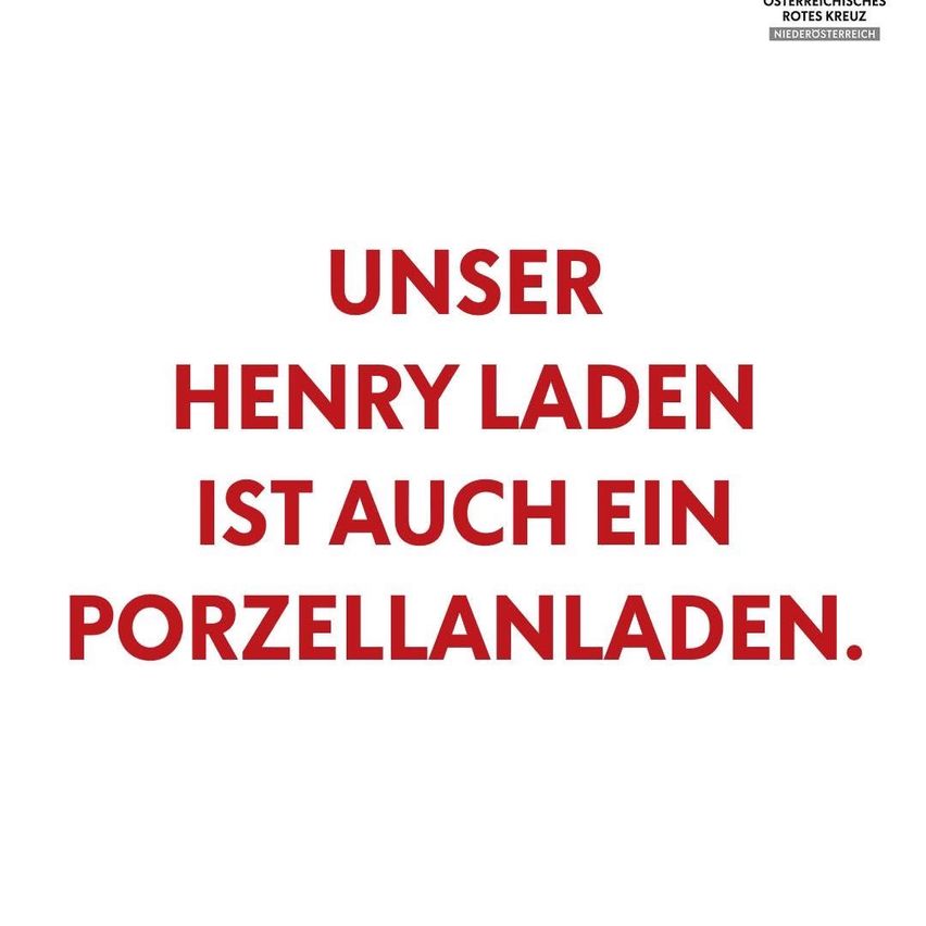 Ein weißes Plakat mit rotem Text lautet 'UNSER HENRY LADEN IST AUCH EIN PORZELLANLADEN'. Der Text ist fett und scheint Teil einer Werbung oder eines Werbematerials zu sein.