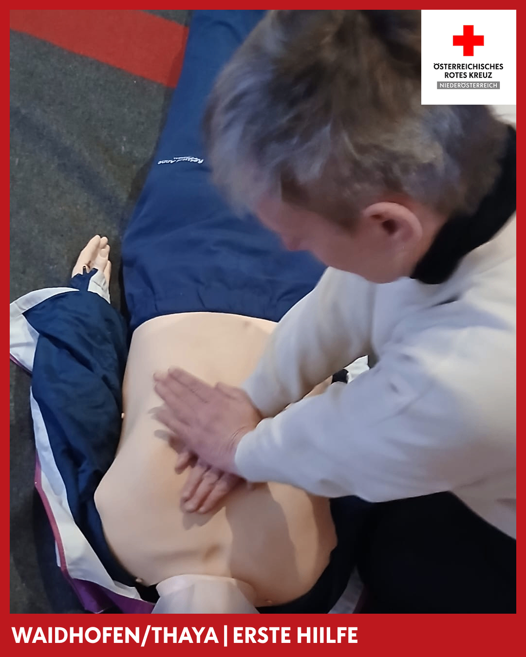 Ein Mann übt CPR an einem Dummy, der auf einer blauen Decke liegt. Seine Hände liegen auf der Brust des Dummies.