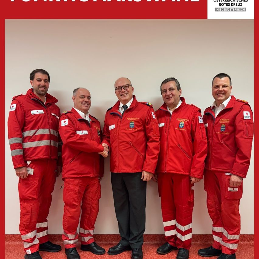 Five men in red uniforms, possibly from the Austrian Red Cross, stand together with smiles on their faces. One man in a black suit stands in the center.