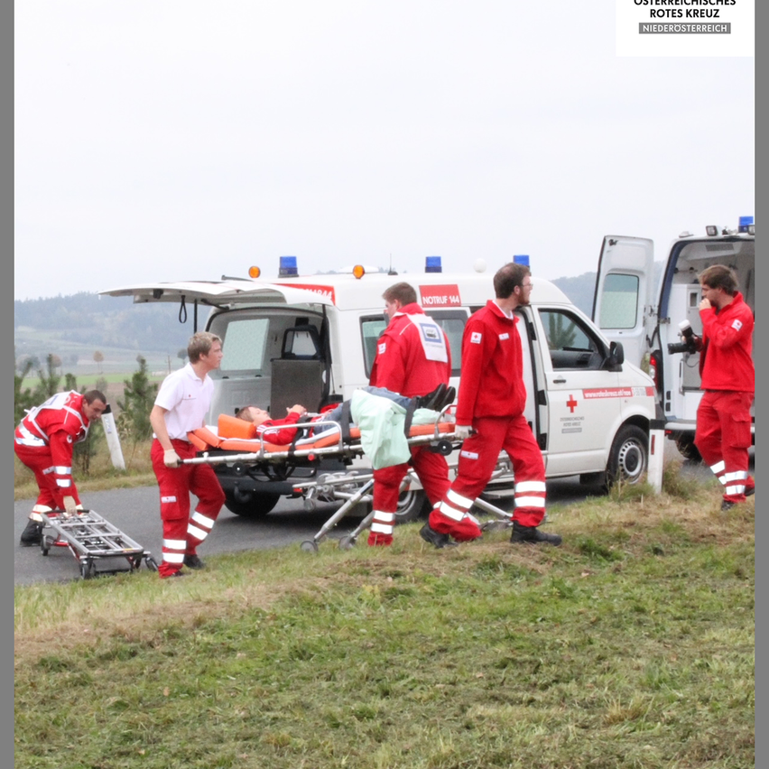 Emergency workers are carrying a person on a stretcher near an ambulance. The person is lying on a stretcher. The ambulance has an open door.