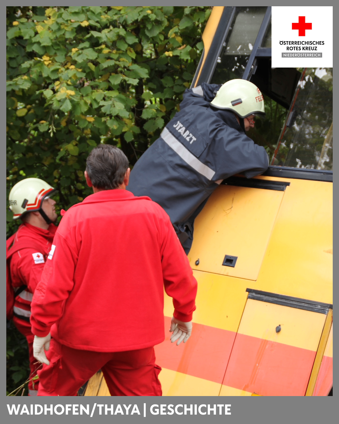 A group of firefighters in red uniforms stand near a yellow and orange vehicle. One firefighter leans out the window.