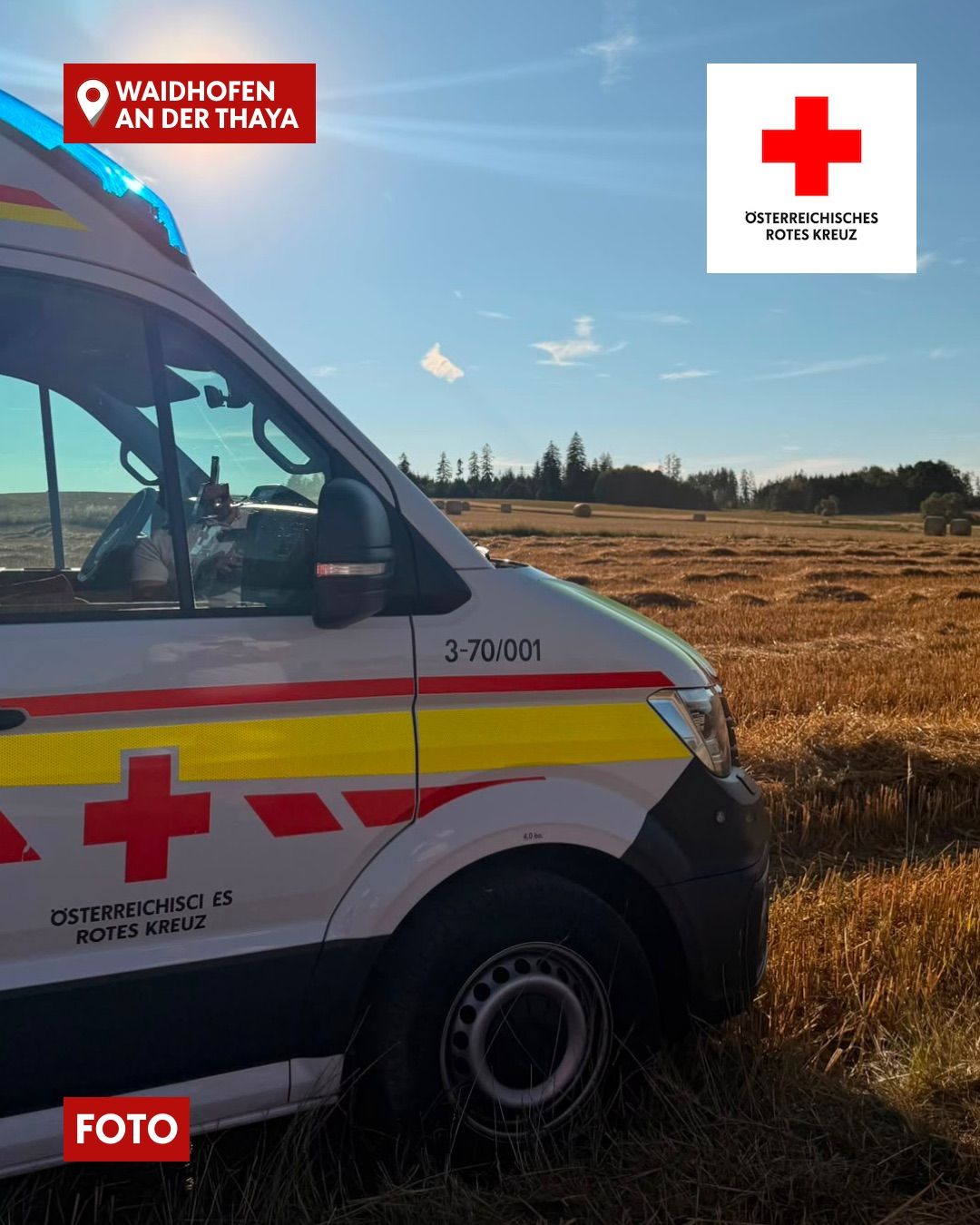 Ein österreichischer Rotkreuz-Ambulanzwagen mit der Nummer 3-70/001 steht auf einem Grasfeld mit klarem blauen Himmel im Hintergrund.