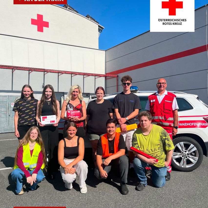 Eine Gruppe von Menschen in Sicherheitswesten und Brillen posiert für ein Foto vor einem weißen Krankenwagen mit einem roten Kreuz auf der Seite.