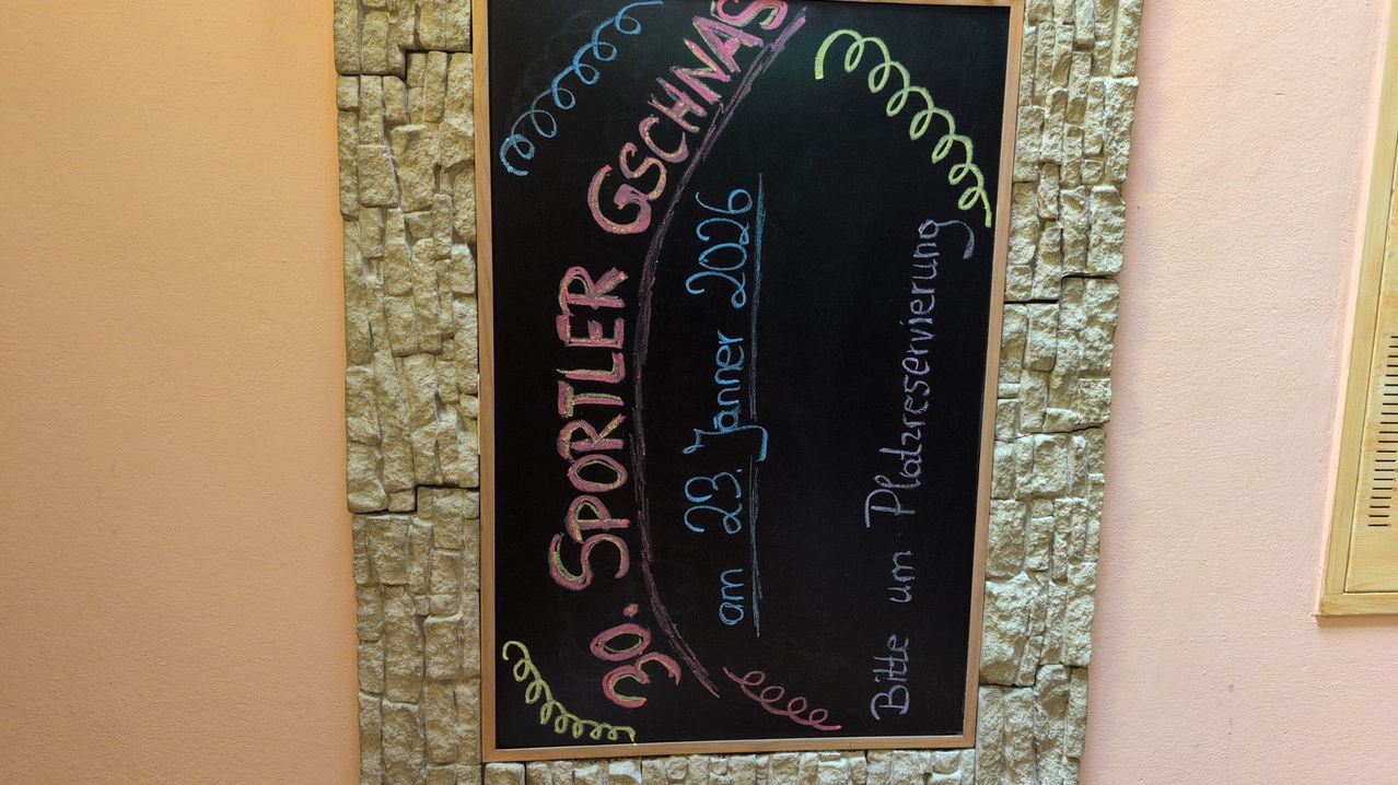 Eine Tafel mit bunter Kreideschrift auf einer Steinmauer. Es steht 'Sportler Geschnas 2006' und 'am 23. Januar 2006' mit dekorativen Schwüngen. Darunter steht 'Bittle um Platzerverierung'.