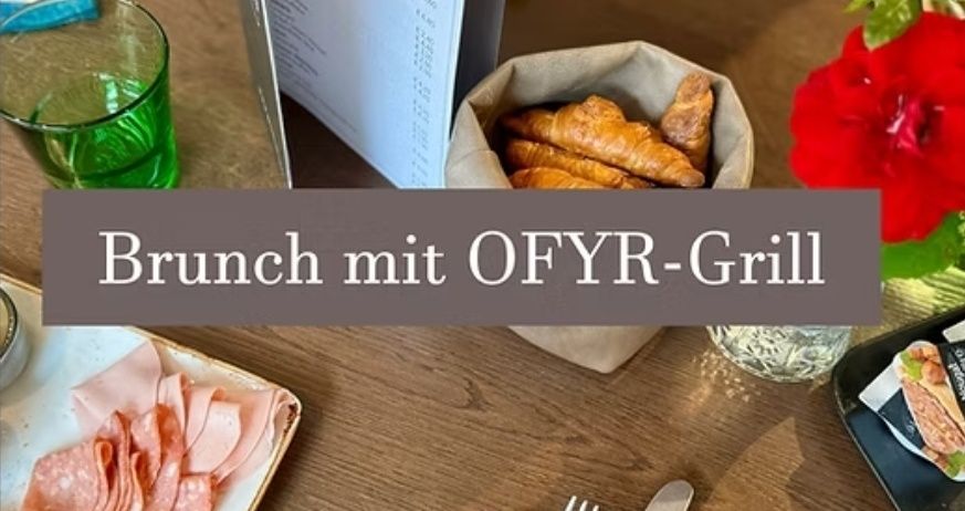 Ein Holztisch zeigt ein Teller mit geschnittenem Fleisch, einem Messer, einer Gabel und einem Blumenvase. Ein Menükarte, ein Glasbecher und ein Korb mit Brot sind ebenfalls vorhanden. Die Worte 'Brunch mit OFYR-Grill' sind auf dem Bild geschrieben.