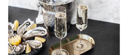 Schaumweingläser mit Blasen stehen auf einem metallischen Tablett neben einem Eimer mit Eis mit einer Champagnerflasche und einem Teller mit Austern.