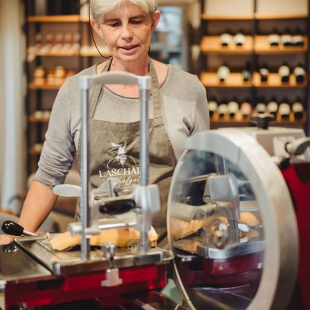 Eine Frau in einem Laschai-Schürze benutzt einen Fleischschneider, um ein Brot in einem Geschäft zu schneiden.